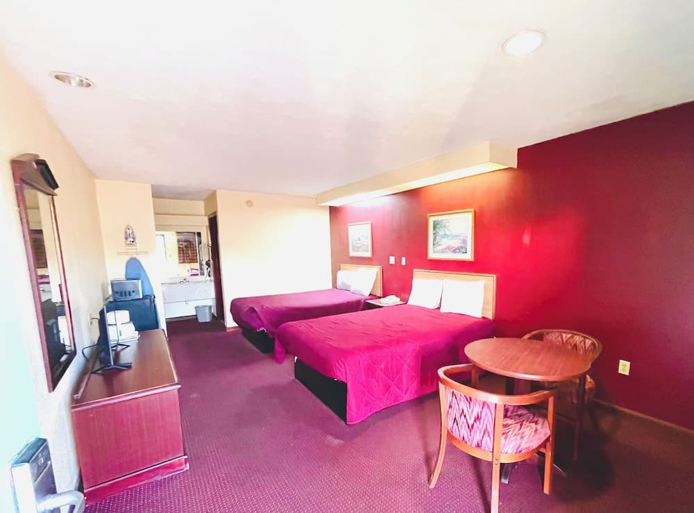 A cozy hotel room with vibrant red walls, two neatly made beds, a small dining table, and a desk area offers a comfortable stay for travelers seeking relaxation and convenience.