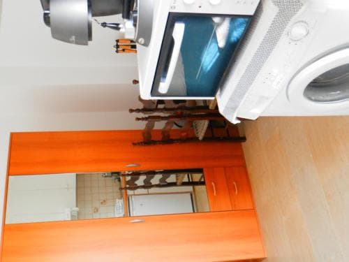 A cozy apartment kitchenette features an orange cabinet with mirrored doors, a washing machine, and a microwave, creating a functional and compact space ideal for short-term travelers seeking efficiency.