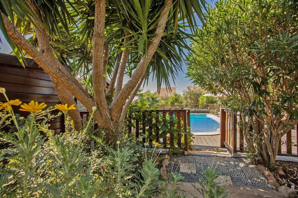 A serene tropical garden pathway framed by lush greenery and vibrant yellow flowers leads to a tranquil poolside retreat, ideal for vacationers seeking relaxation in a private oasis.