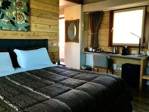A cozy cabin-style hotel room with wooden walls, a neatly made bed, and a small desk by the window, ideal for travelers seeking a warm and rustic retreat.