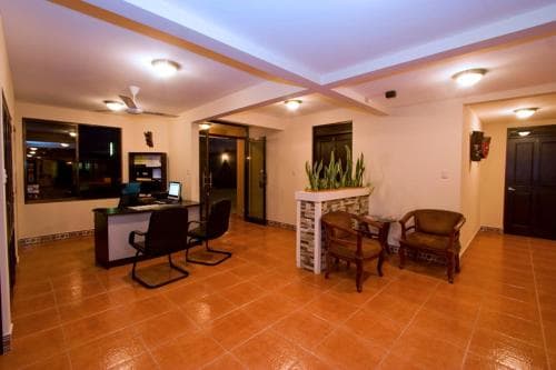 A warmly lit hotel lobby features terracotta flooring, cozy seating, a reception desk with a computer, and decorative plants, creating an inviting atmosphere ideal for travelers seeking comfort and convenience.