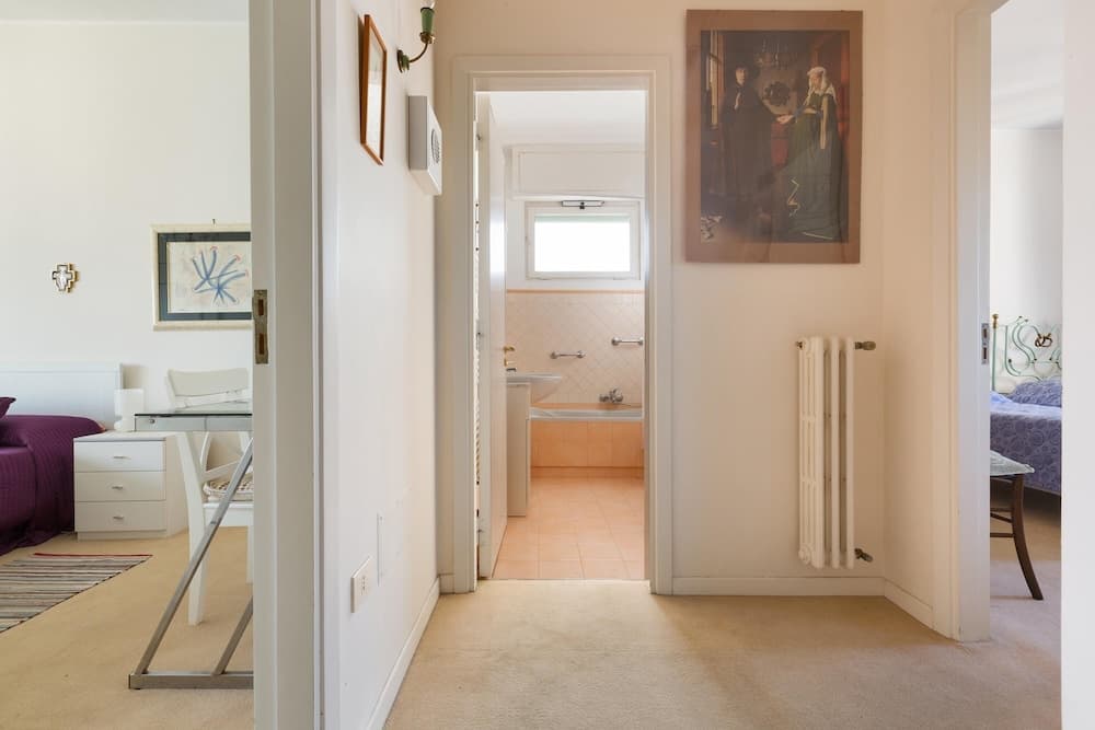 A cozy apartment hallway leads to a bathroom with peach tiles, framed by artwork and a radiator, ideal for travelers seeking a charming and intimate stay.