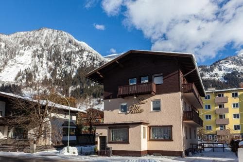 A cozy alpine lodge with balconies stands against a backdrop of snow-capped mountains under a bright blue sky, ideal for winter retreats and ski vacations.