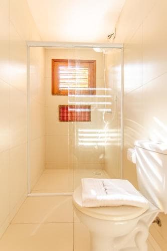 A bright, modern bathroom features a glass-enclosed shower with colorful mosaic tiles, a neatly folded towel on the toilet, and a window with wooden blinds, ideal for travelers seeking clean and stylish accommodations.