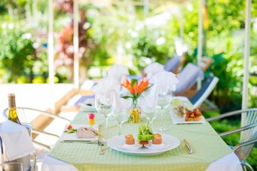 A serene outdoor dining setup with vibrant flowers and neatly arranged plates invites travelers to enjoy a leisurely meal amidst lush greenery, perfect for a relaxing vacation experience.