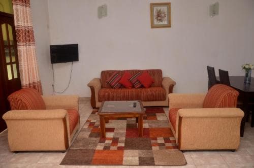 A cozy living room with warm-toned furniture, patterned rugs, and a flat-screen TV creates an inviting atmosphere, ideal for travelers seeking comfort in a homestay or guesthouse setting.