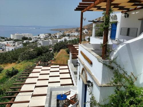 A serene coastal village scene features white-washed buildings with blue accents, wooden balconies, and lush greenery overlooking the calm sea, ideal for travelers seeking a tranquil Mediterranean retreat.
