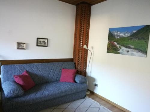 A cozy living room with a blue sofa adorned with pink pillows, wooden accents, and a scenic mountain poster creates a serene atmosphere ideal for travelers seeking relaxation in a quaint lodge setting.