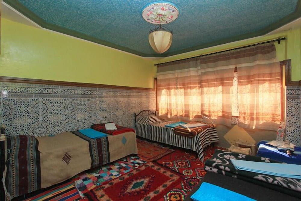 A cozy, vibrant guesthouse room features patterned rugs, traditional textiles, and ornate tiled walls, creating an inviting atmosphere ideal for cultural immersion travelers seeking local charm.