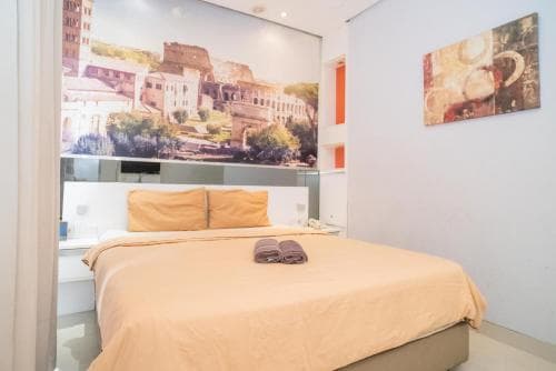 A cozy hotel room features a neatly made bed with beige linens, vibrant wall art depicting historic architecture, and modern decor, ideal for travelers seeking comfort and cultural inspiration.