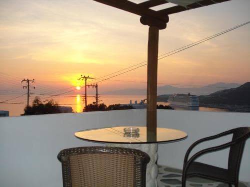 A serene sunset view from a rooftop terrace overlooking the sea, featuring a cozy table and chairs under a pergola, ideal for travelers seeking relaxation and scenic beauty.