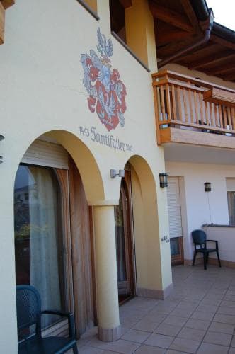 A charming European-style building with arched doorways, a balcony adorned with a floral emblem, and outdoor seating invites travelers to enjoy a cozy retreat in a quaint setting.
