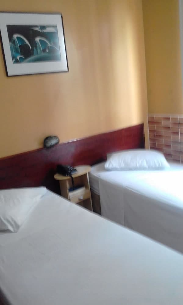 A cozy hotel room features two neatly made beds beside a small wooden nightstand with a phone, set against warm-toned walls adorned with an abstract painting, ideal for travelers seeking a comfortable and simple accommodation.
