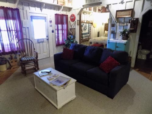 A cozy living room scene with a navy blue couch, red cushions, a white coffee table, and rustic decor creates a warm, inviting atmosphere ideal for travelers seeking a quaint, homey accommodation experience.
