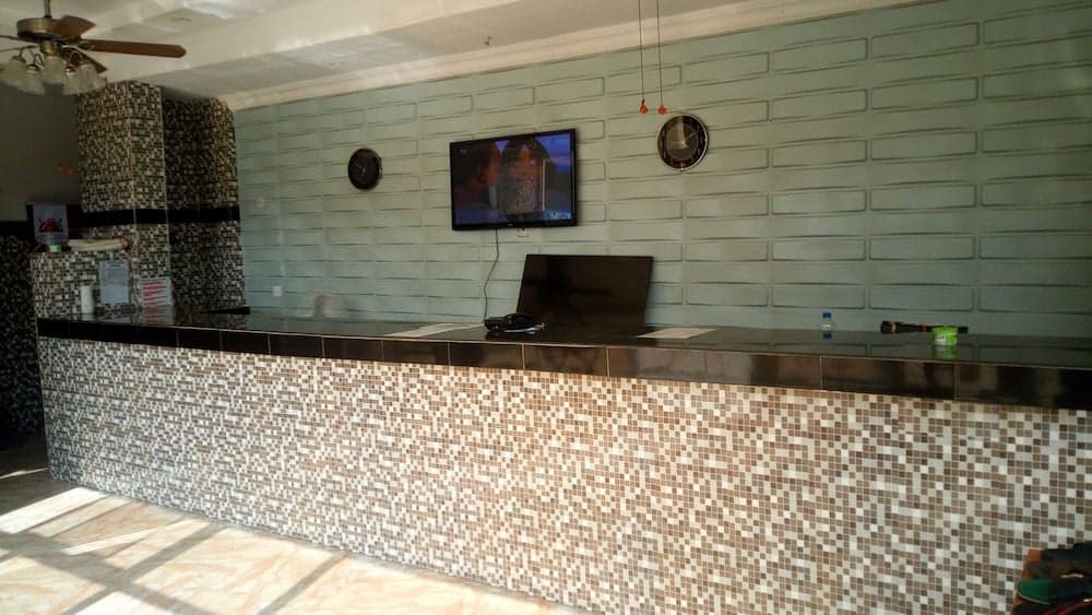 A cozy hotel reception area features a mosaic-tiled counter, a sleek TV on the wall, and a calm ambiance ideal for travelers seeking a welcoming check-in experience.