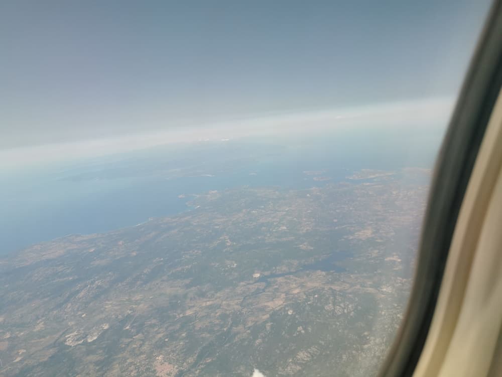 A serene aerial view from an airplane window showcases a vast landscape of green fields, scattered islands, and calm blue waters, ideal for travelers seeking scenic flight experiences.
