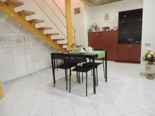 A cozy apartment dining area features a modern table set for breakfast under a staircase, with warm lighting and wooden cabinets, ideal for travelers seeking a comfortable self-catering stay.