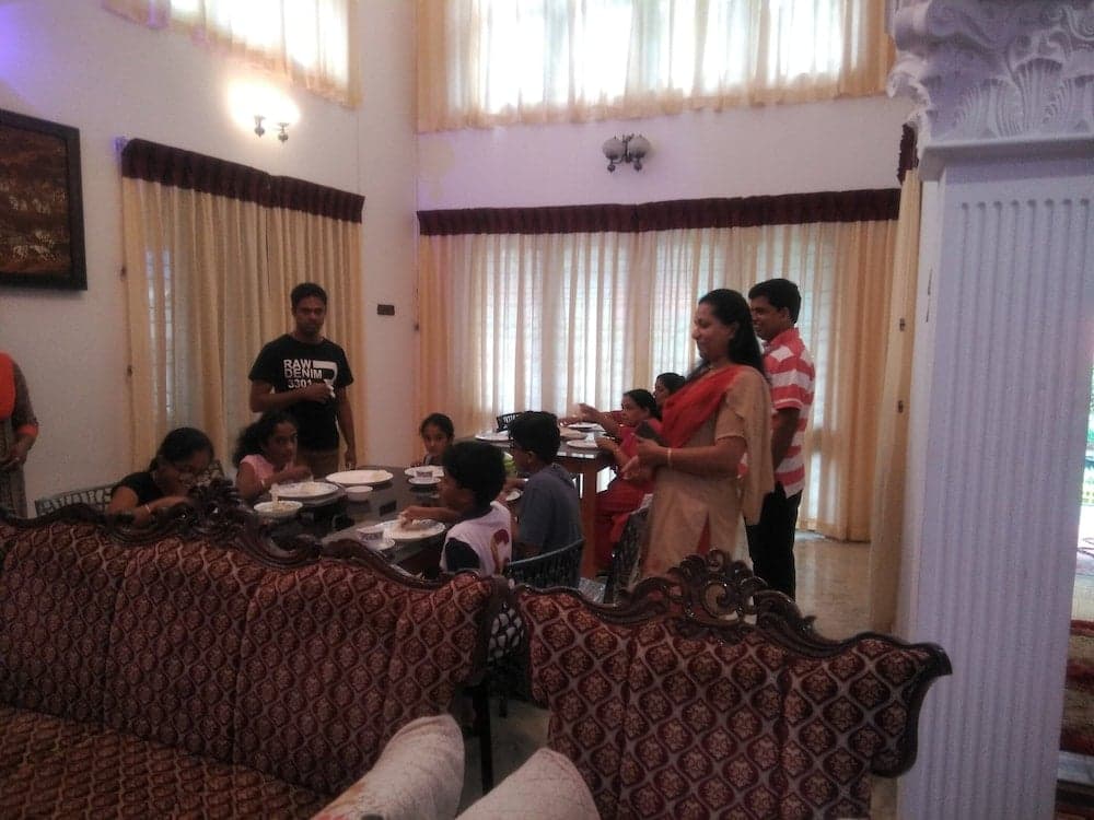 A cozy indoor gathering in a warmly lit living room with patterned sofas, a dining table filled with plates, and people enjoying a meal together, ideal for family-oriented travel experiences.