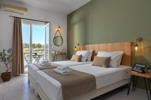 A cozy hotel room with twin beds, a balcony overlooking greenery, modern decor, and warm lighting creates an inviting atmosphere perfect for travelers seeking relaxation and comfort.