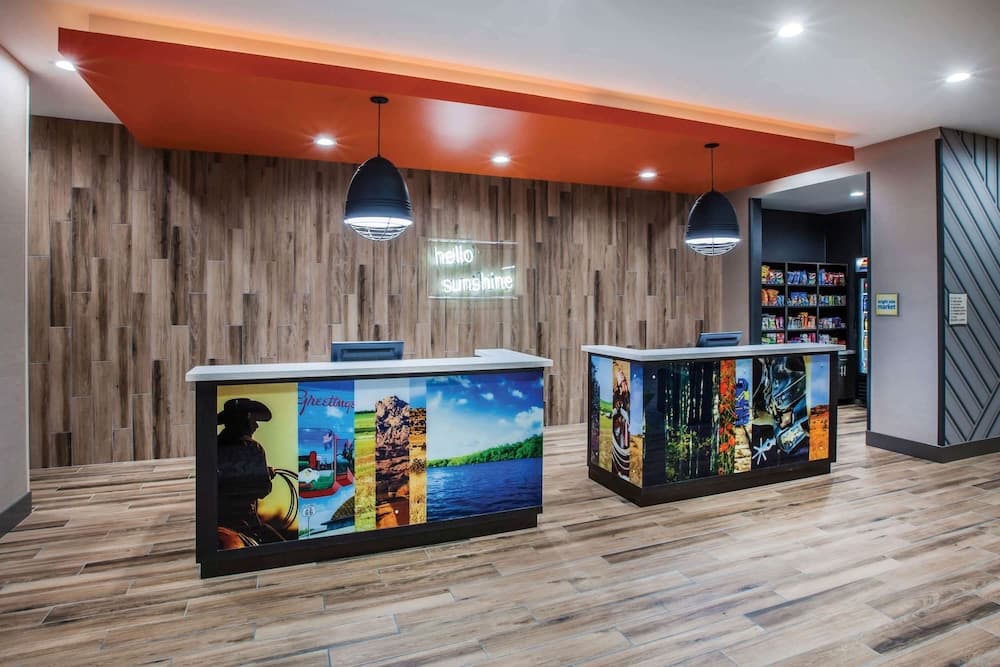 A warmly lit hotel lobby features modern wooden decor, vibrant desk artwork, and a cozy "hello sunshine" sign, ideal for travelers seeking a welcoming atmosphere.
