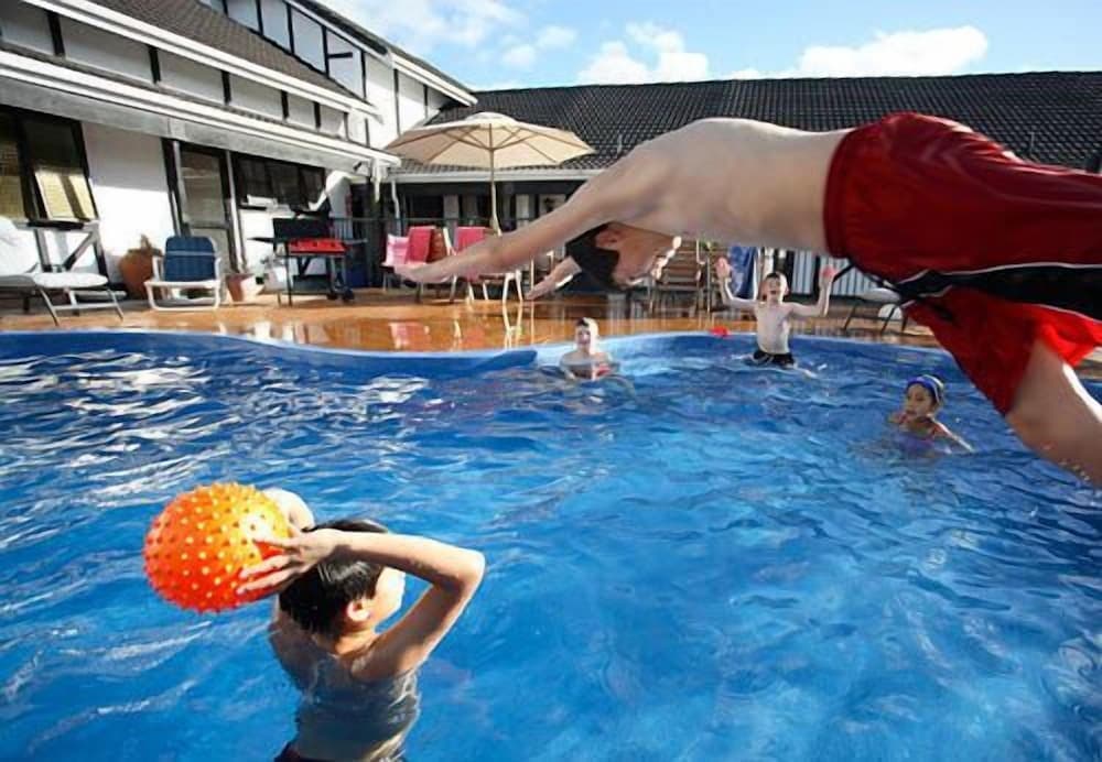 A joyful family dives into a vibrant blue pool surrounded by lounge chairs and umbrellas at a resort, capturing the essence of summer fun and relaxation for travelers seeking family-friendly vacation spots.