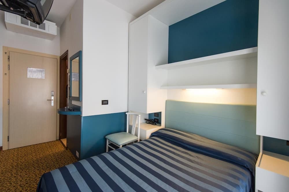 A cozy hotel room features a neatly made bed with striped bedding, a compact desk area, and modern storage units, ideal for travelers seeking comfort in a compact space.