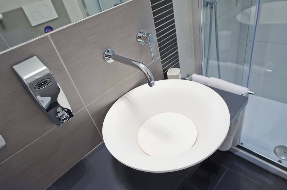 A modern bathroom features a sleek white vessel sink on a dark countertop, complemented by a chrome faucet and a glass-enclosed shower, ideal for travelers seeking contemporary design in accommodations.