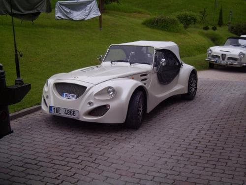 A sleek white sports car parked on a cobblestone driveway amidst lush greenery evokes a serene and luxurious atmosphere, ideal for travelers seeking a classic automotive experience in a picturesque setting.