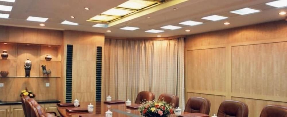 A warmly lit conference room with wooden paneling, leather chairs, decorative shelves, and floral arrangements offers an inviting space for professional meetings and business travelers seeking a serene environment.