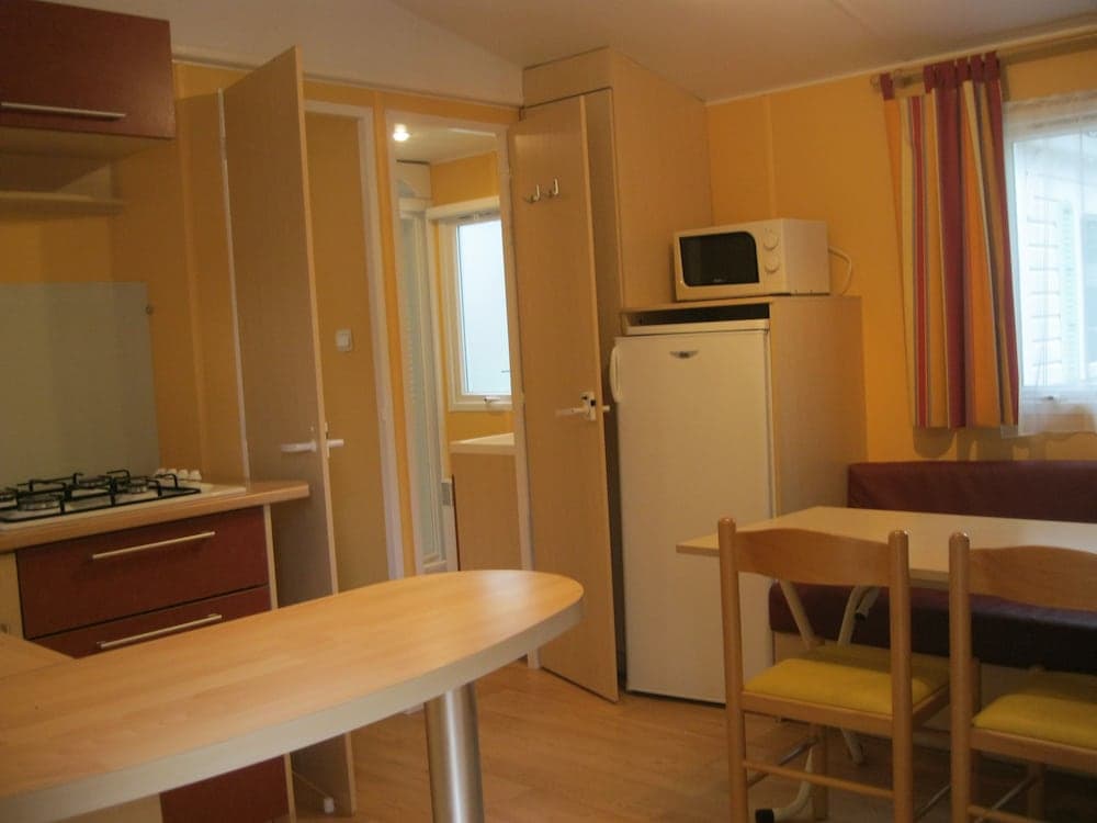 A cozy, compact apartment interior features warm yellow walls, wooden furniture, a small kitchenette with a stove, and a dining area by the window, ideal for travelers seeking a comfortable and functional short-term stay.