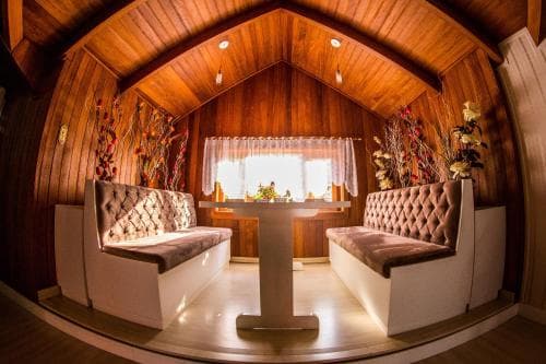 A cozy, warmly-lit wooden interior with tufted benches facing a central table under a vaulted ceiling, ideal for intimate gatherings or unique dining experiences.