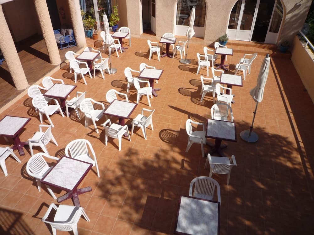 A sunlit outdoor patio with neatly arranged tables and chairs casts inviting shadows, ideal for travelers seeking a relaxing café or restaurant setting.