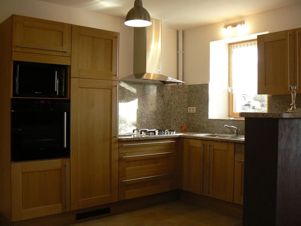 A cozy kitchen with wooden cabinets, granite countertops, and natural light from a window creates a warm atmosphere ideal for home cooking enthusiasts.