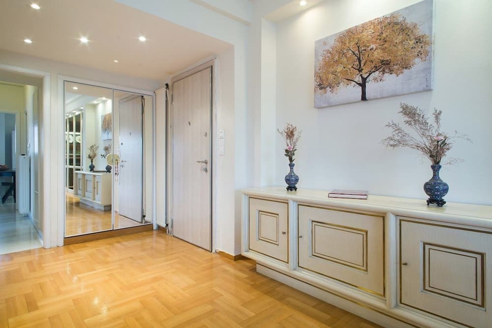 A cozy apartment hallway features warm wooden flooring, elegant vases on a cream-colored cabinet, and a serene tree painting, ideal for travelers seeking a comfortable urban retreat.
