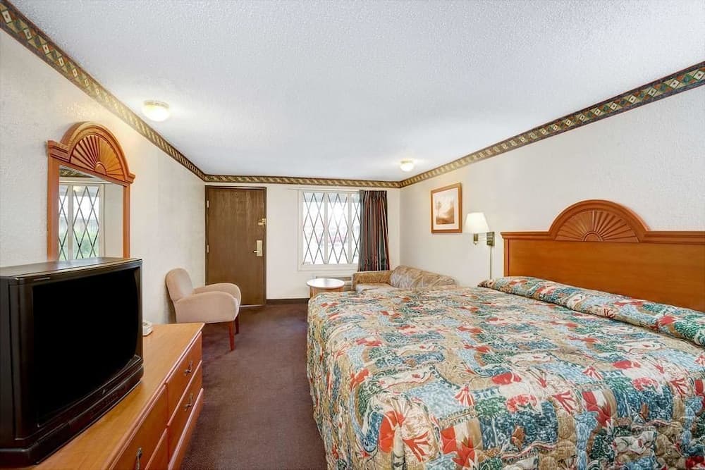 A cozy hotel room features a floral bedspread, wooden furnishings, and a vintage TV, creating a warm and inviting atmosphere ideal for travelers seeking comfort and relaxation.