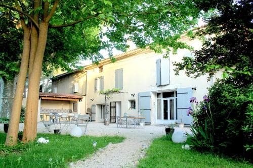 A serene courtyard with lush greenery frames a charming European-style villa featuring outdoor seating, evoking a tranquil vacation retreat ideal for relaxation and leisure.