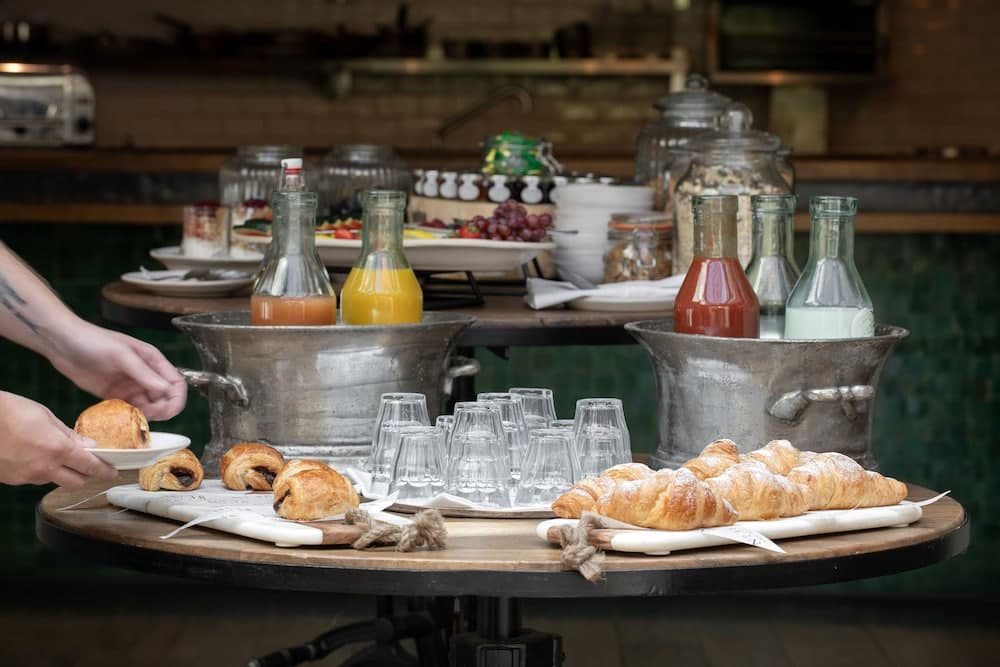 A cozy café scene features a rustic table laden with fresh croissants, juices in vintage bottles, and an assortment of breakfast items, creating a warm and inviting atmosphere perfect for a leisurely morning outing.