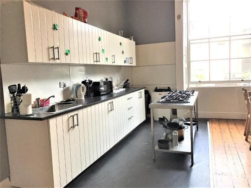 A bright, modern kitchen with white cabinets, black countertops, and ample natural light through large windows creates an inviting atmosphere ideal for culinary enthusiasts seeking a functional space for cooking and entertaining.