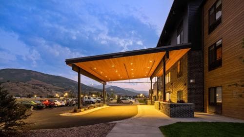 A serene evening at a modern lodge with a warmly lit wooden awning, set against a backdrop of distant mountains, ideal for travelers seeking a cozy retreat in a scenic location.