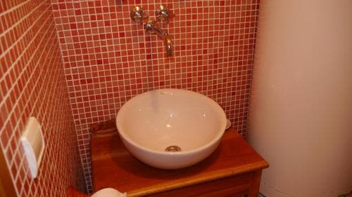 A cozy bathroom with vibrant red mosaic tiles features a sleek white bowl sink on a wooden vanity, ideal for travelers seeking a stylish yet functional accommodation space.