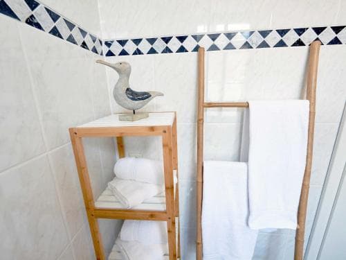 A serene bathroom scene features white tiled walls adorned with a blue diamond-patterned border, a wooden towel rack holding crisp white towels, and a decorative seagull figurine on a shelf, ideal for travelers seeking a clean and coastal-inspired accommodation.