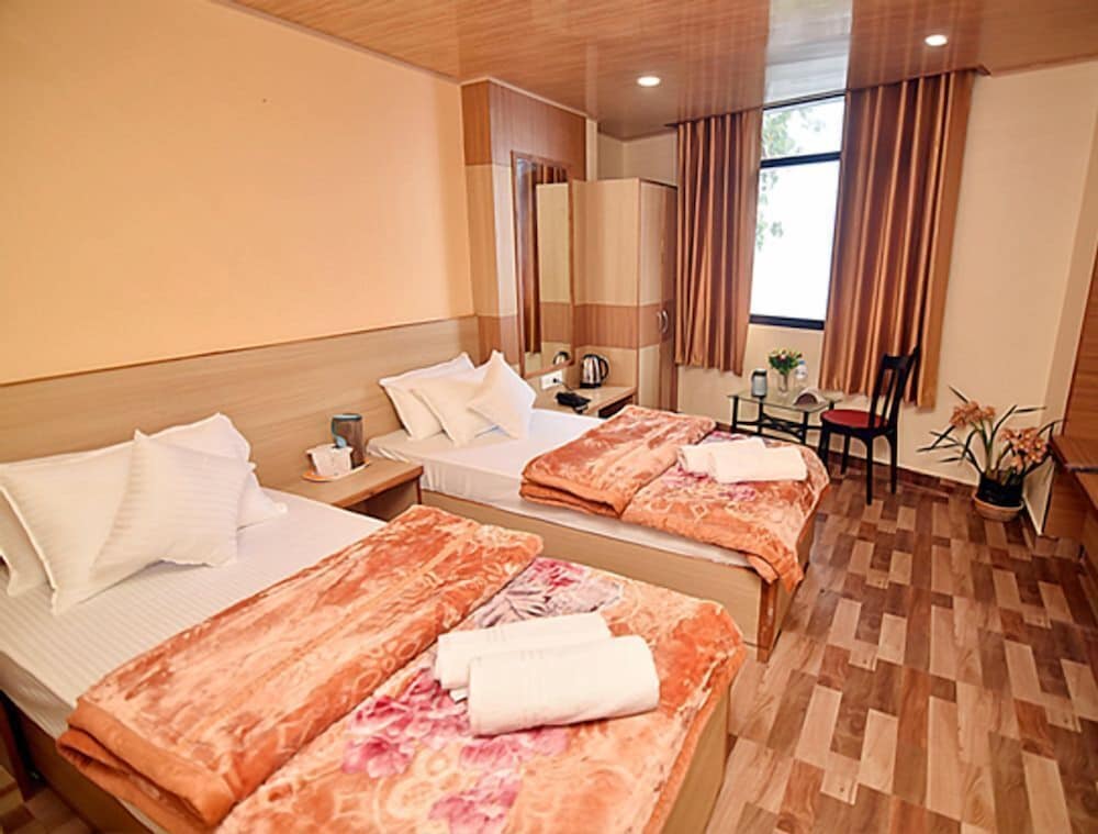 A cozy hotel room with two neatly made beds, warm wooden decor, and a small seating area by the window, ideal for travelers seeking comfort and relaxation.