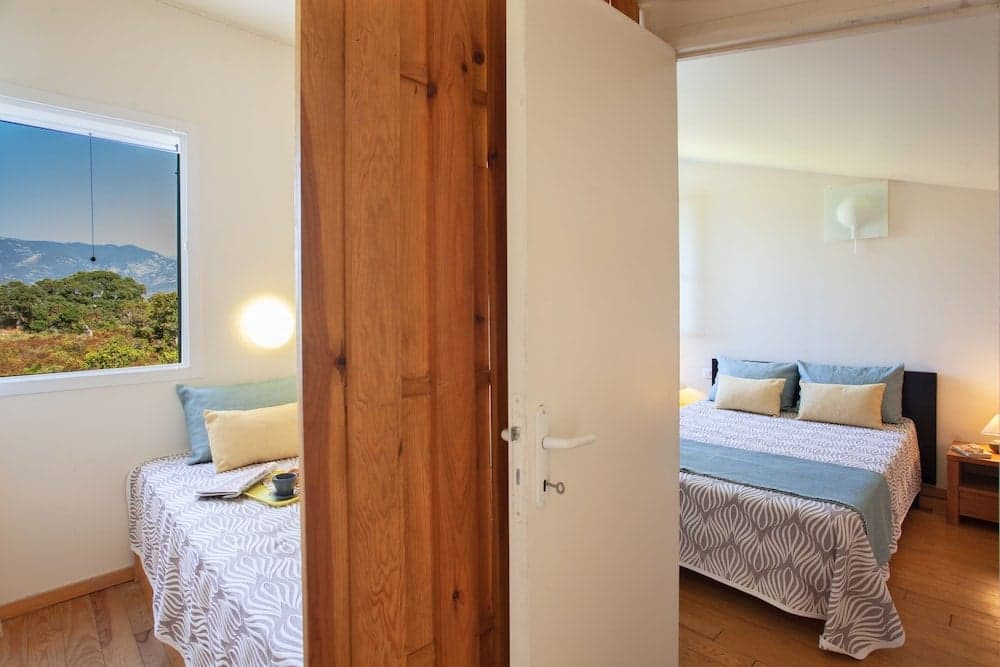 A cozy bedroom with wooden floors, soft bedding, and a scenic mountain view through the window invites travelers seeking relaxation in a serene retreat.