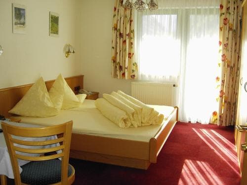 A cozy hotel room features a neatly made bed with rolled towels, floral curtains, and warm sunlight streaming through the window, creating an inviting atmosphere ideal for travelers seeking comfort and relaxation.
