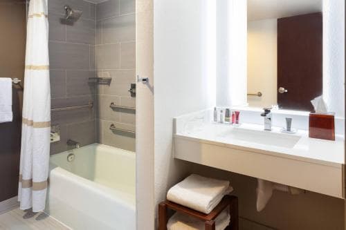 A modern hotel bathroom features a sleek bathtub, tiled walls, a spacious vanity with toiletries, and neatly folded towels, creating a clean and inviting atmosphere ideal for travelers seeking comfort and convenience.