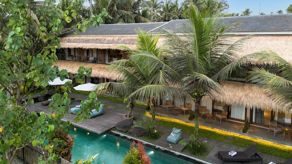 A serene tropical resort features lush palm trees, a tranquil poolside area with lounge chairs, and thatched-roof villas, ideal for a relaxing vacation getaway.