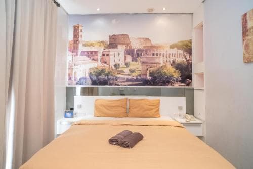 A cozy hotel room features a neatly made bed with yellow linens under a large mural of ancient Roman ruins, creating an inviting atmosphere for travelers seeking comfort and cultural inspiration.