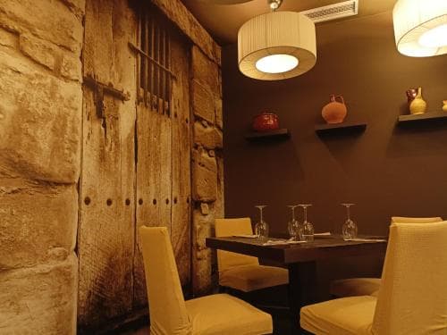 A cozy restaurant corner features warm lighting, rustic stone walls, modern yellow chairs, and elegant glassware, ideal for intimate dining experiences.