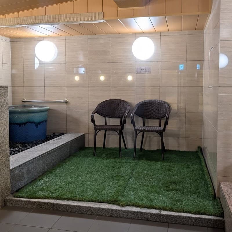 A serene indoor relaxation area at Shinsaibashi ARTY Inn in Osaka features artificial grass flooring, wicker chairs, and a tranquil water feature, ideal for travelers seeking a peaceful retreat.