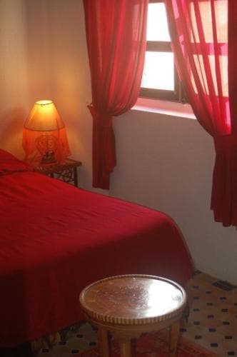 A cozy bedroom with vibrant red curtains, bedding, and a patterned floor exudes warmth and charm, ideal for travelers seeking a serene and culturally rich accommodation experience.